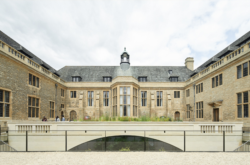 Historic stone building in a horseshoe style with large windows facing onto a landscaped courtyard. Using natural stone for the property.