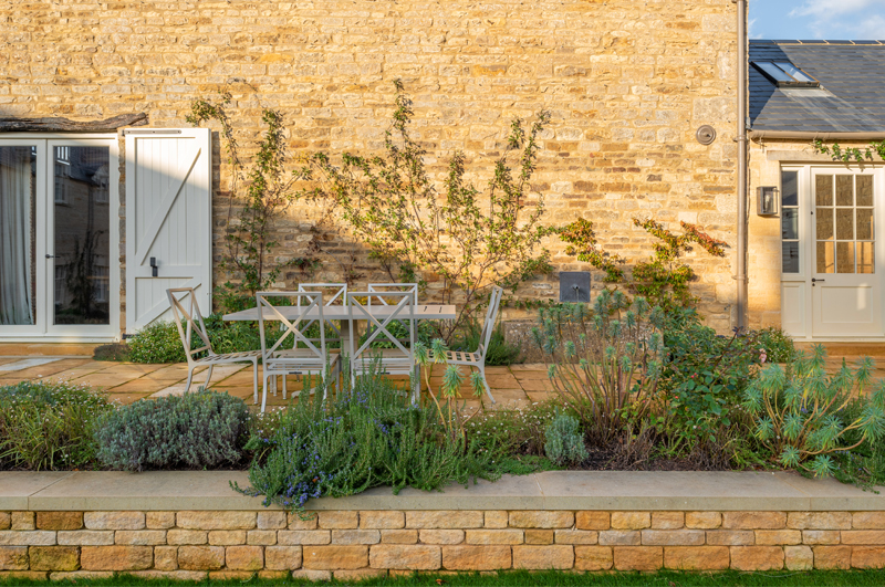 Countryside home with natural stone walls, stone paving and a white table and chairs on the patio.